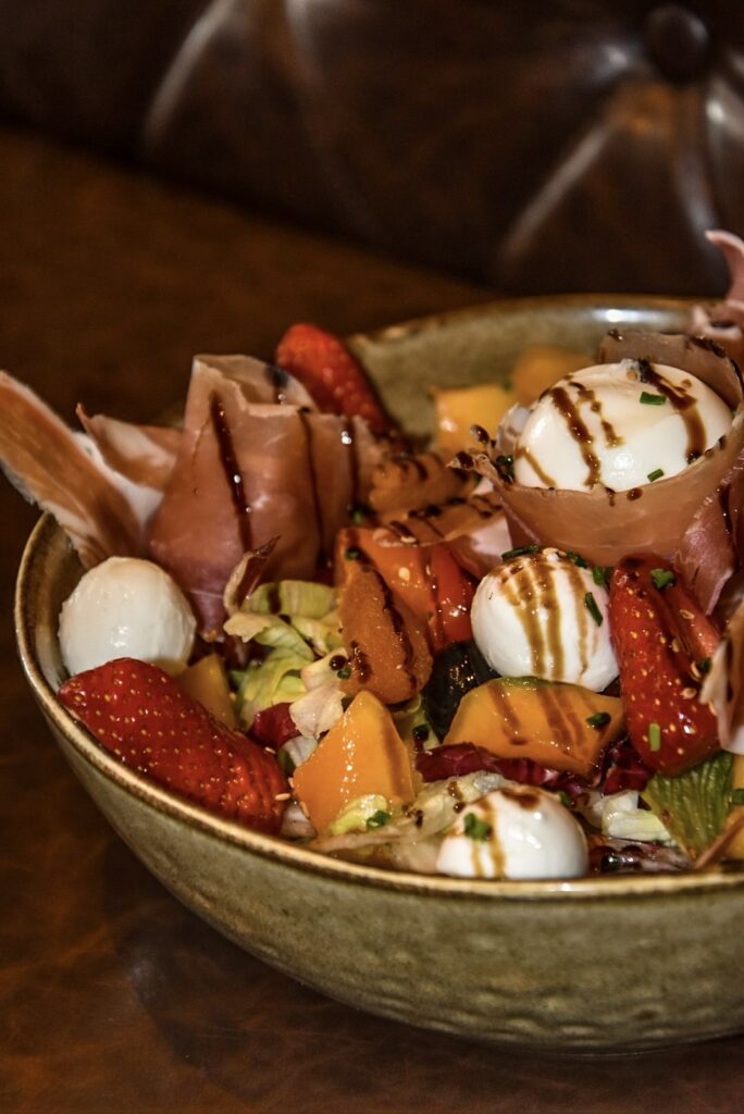 La salade estivale du Watson's Pub est composée de la salade iceberg, tomates cerises, melon, mozzarella, oeuf mollet, jambon de montagne, olives noires, fraises, sésame grillé, vinaigrette à l'estragon